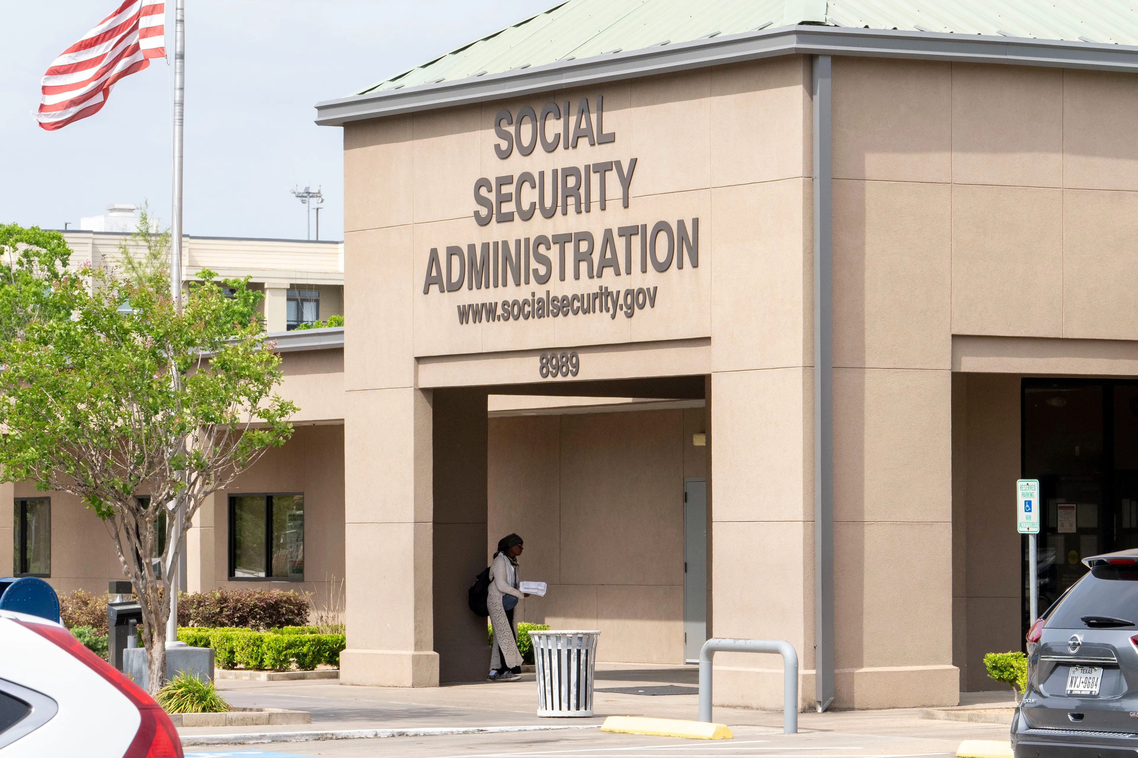 People walking into a local Social Security office building during daytime, with the agency sign visible near the door